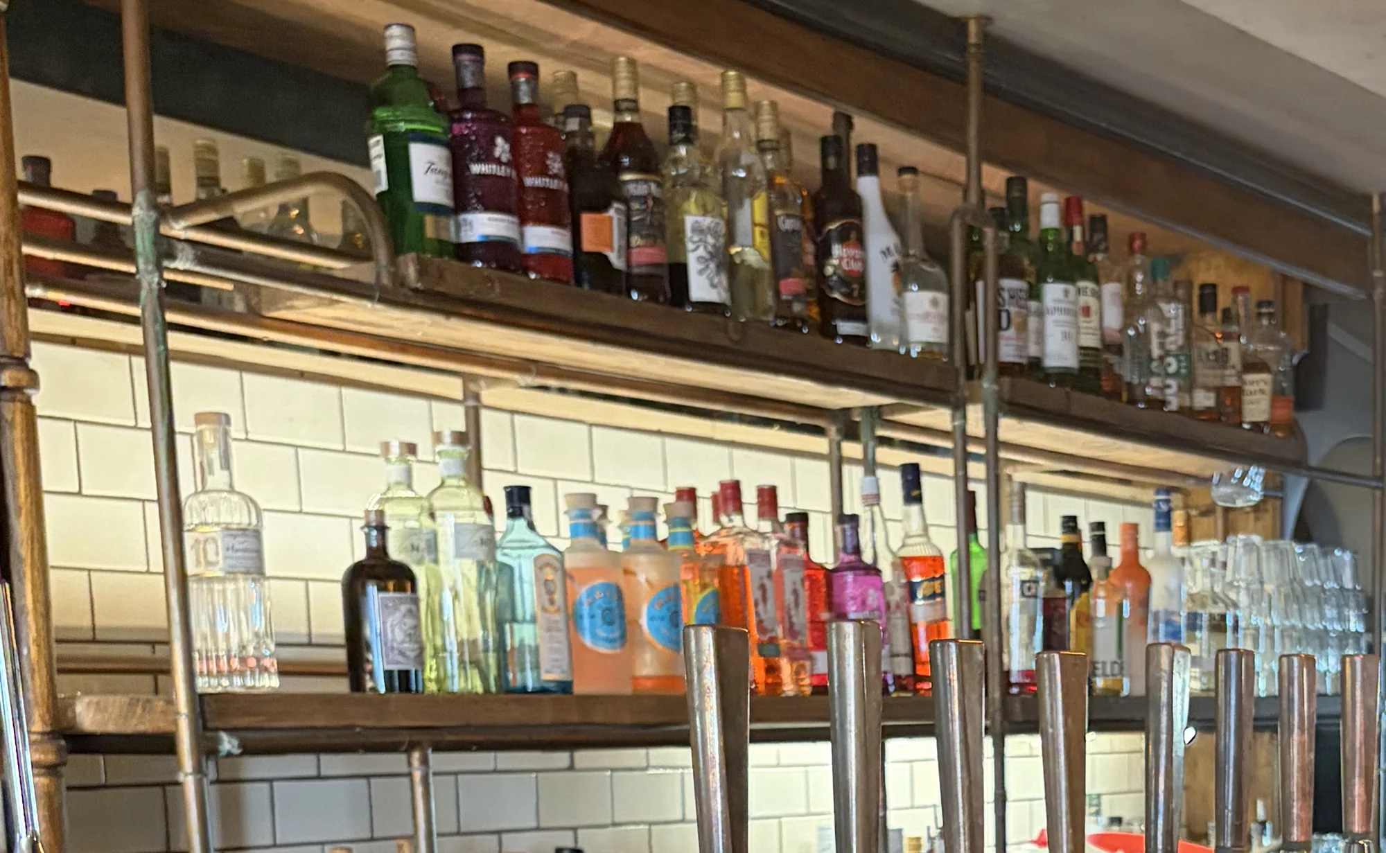 The back bar at The Pullman: copper-pipe shelves of gin, whisky and rum bottles against white tiles