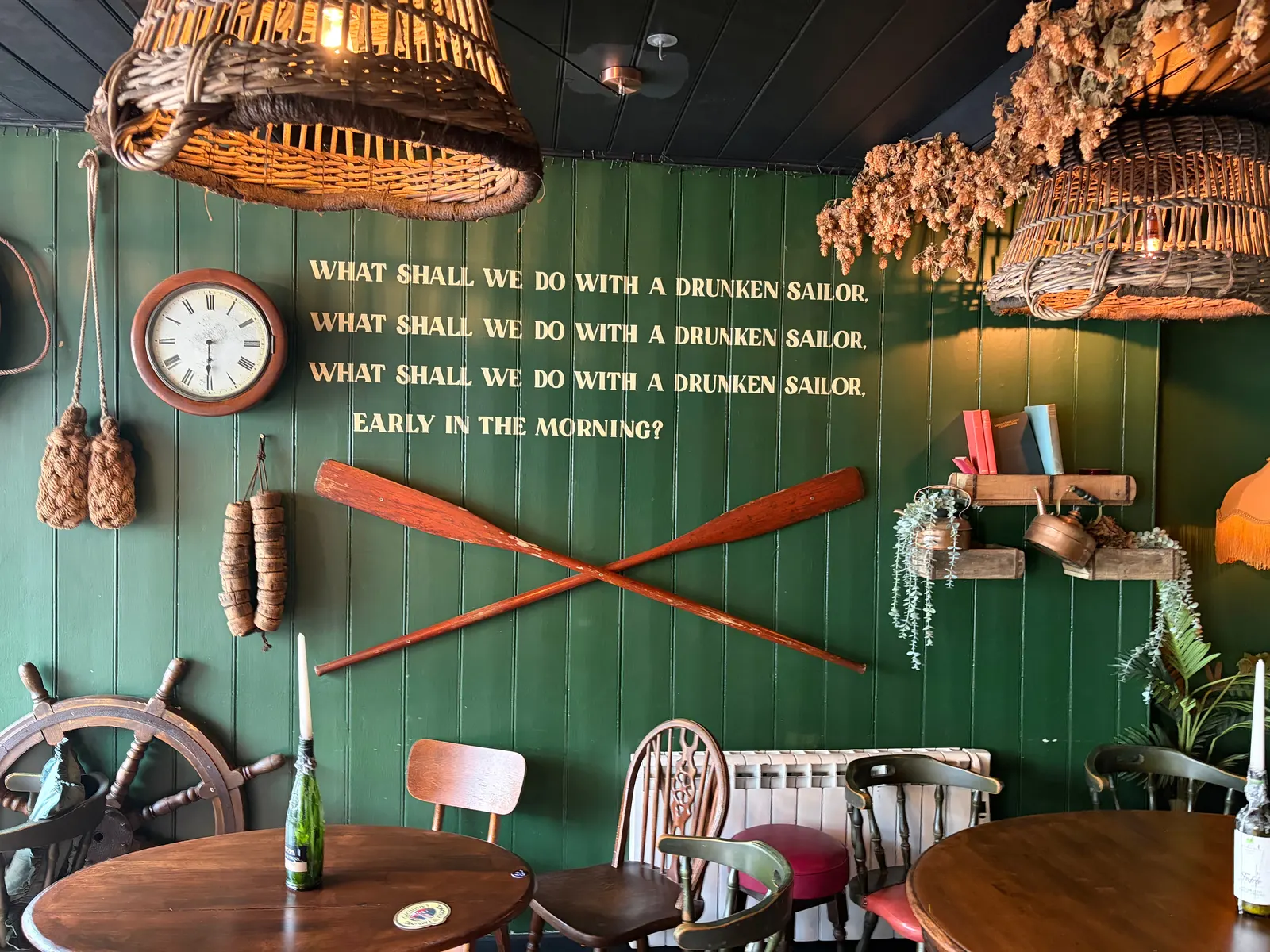 The green feature wall at The Ship Inn, Sandgate, with a clock, crossed oars and a ship's wheel