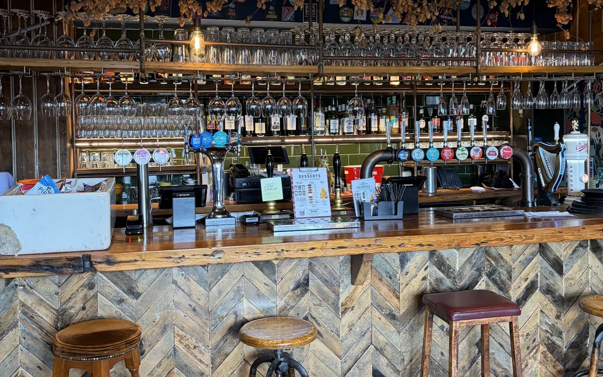 The bar at Harbour Inn: a herringbone-panelled counter with stools, beer taps and a back bar of glasses and bottles under hanging hops